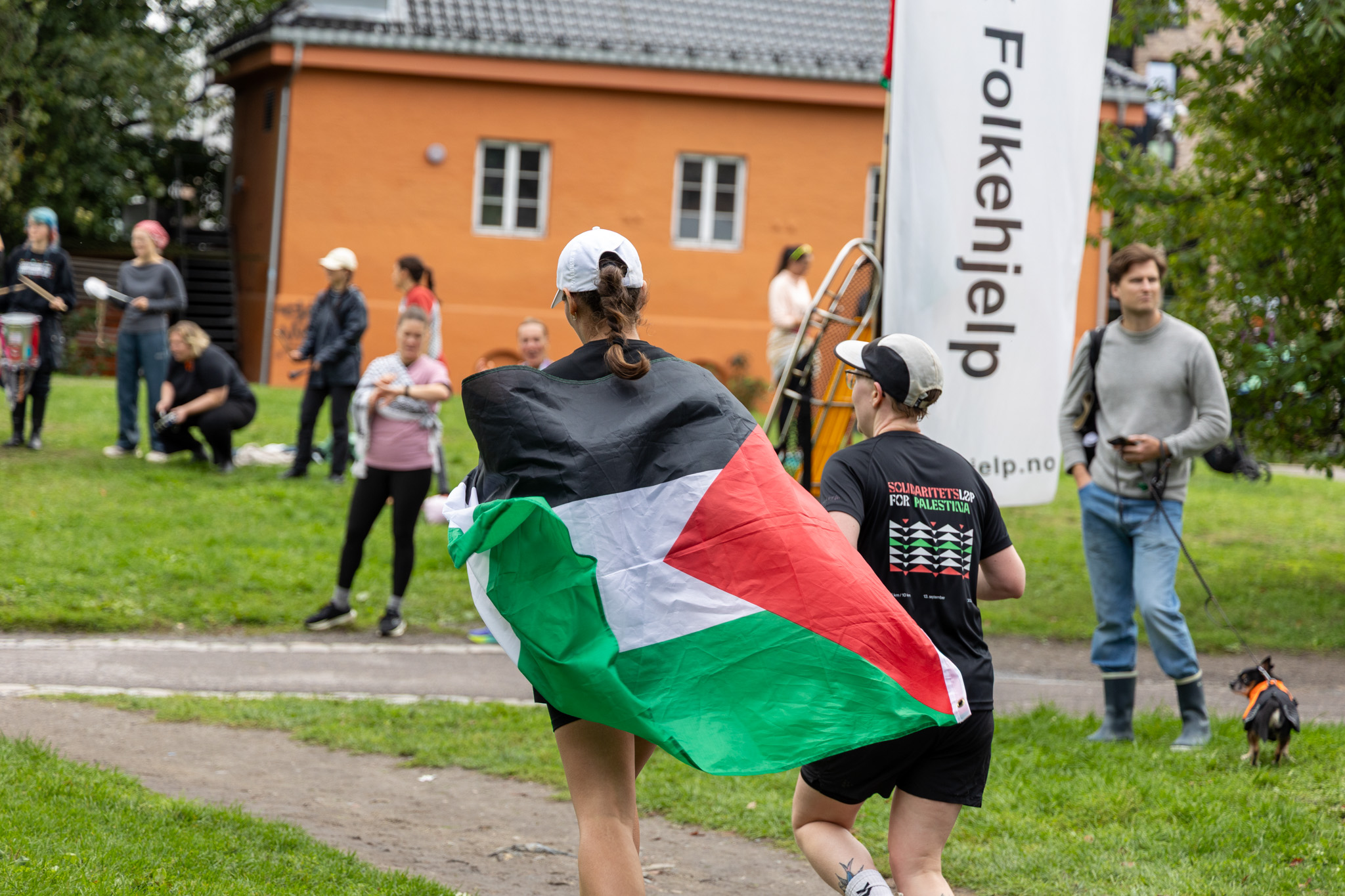 To personer jogger mot mål, én med palestina-flagg over skuldrene. Sett bakfra.