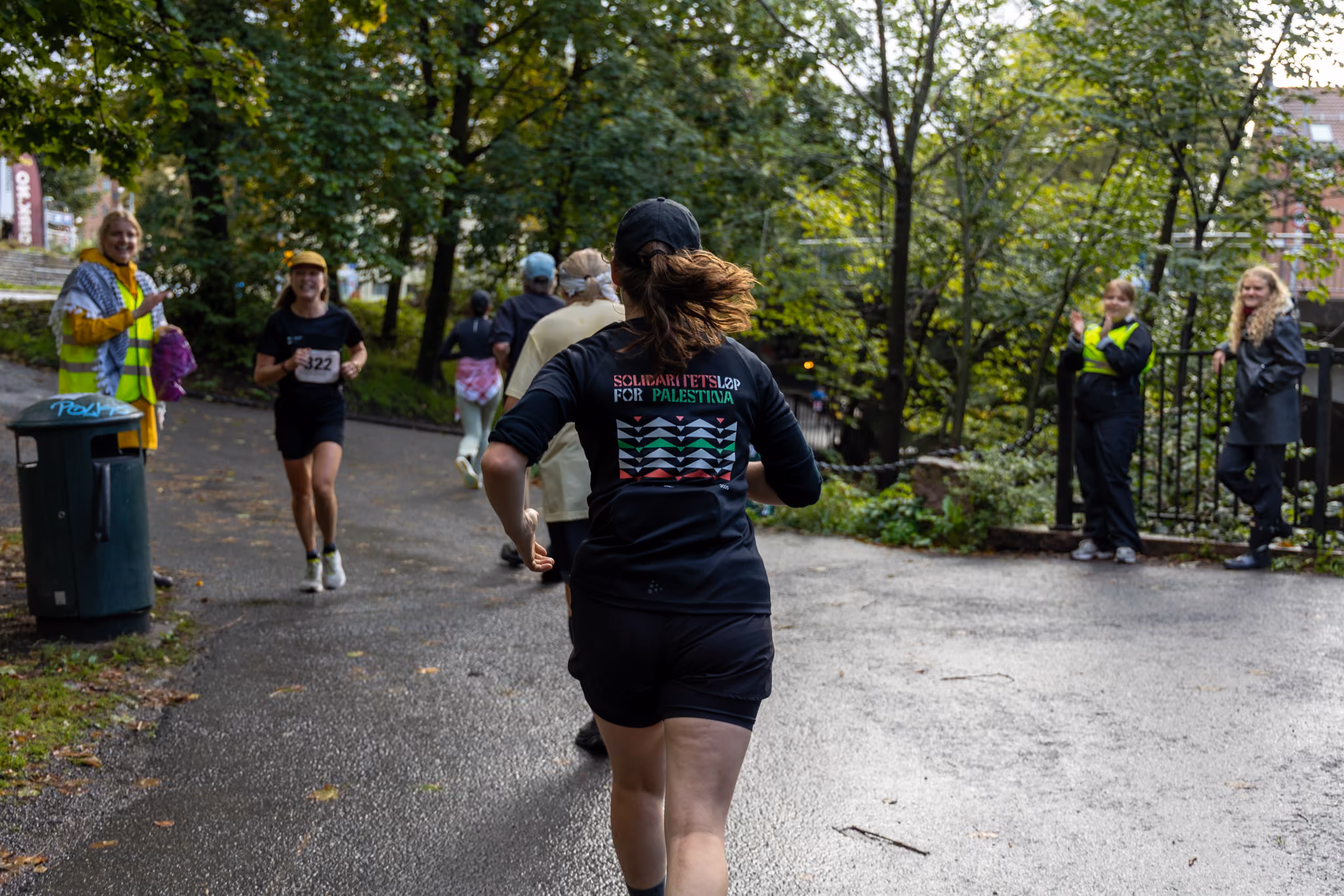 En jogger sett bakfra løper med t-skjorte fra Solidaritetsløp for Palestina. Motgående løper på siden.