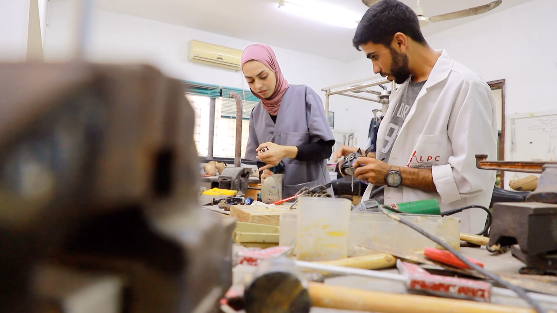 Two people in medical uniform working with tools, assembling prosthetic limbs.