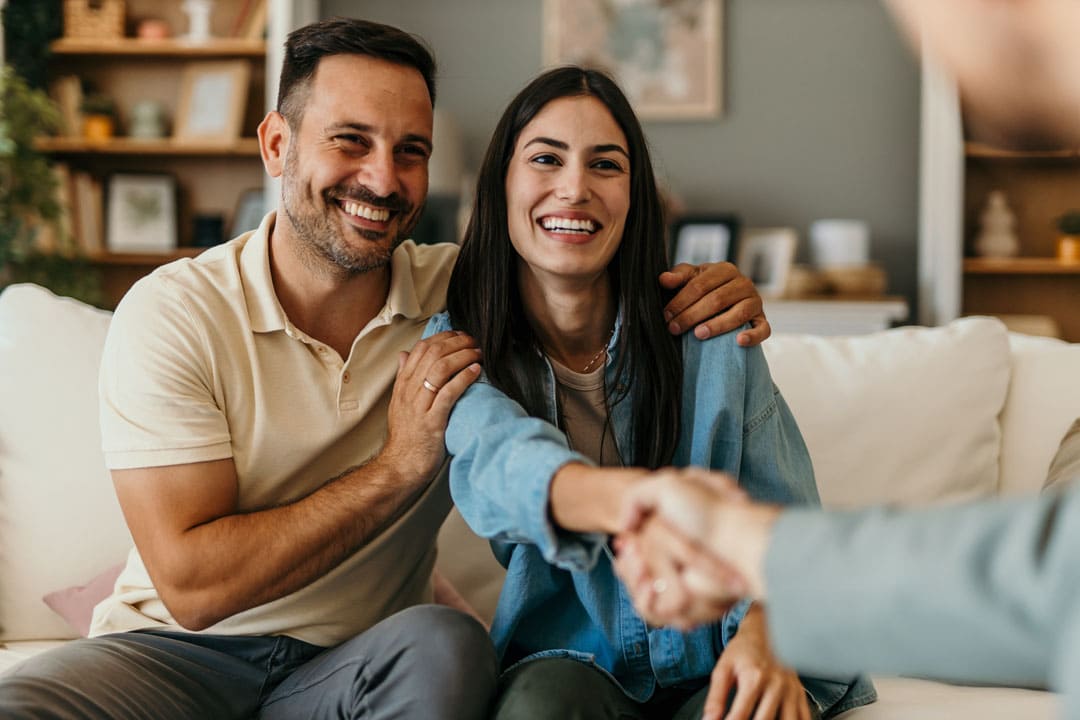 Homeowners smiling and shaking hands with a contractor after a foundation consultation