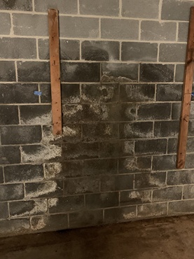 Cinder block basement wall with efflorescence and moisture stains, indicating water intrusion and need for waterproofing
