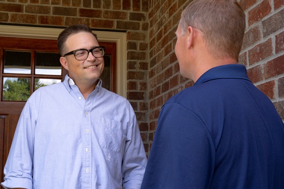 Homeowner smiling and talking with technician at front door during foundation inspection consultation