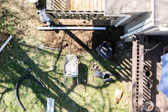 Technicians installing exterior PVC drainage pipe in a trench along house for basement waterproofing and foundation drainage.