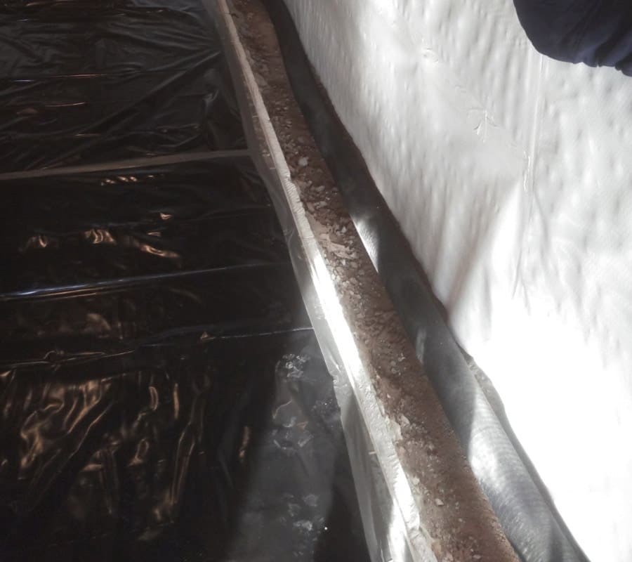 Perimeter drainage trench with gravel and wrapped drain pipe beside white wall liner and black vapor barrier