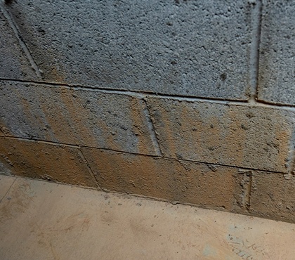 Cinder block basement wall with mineral stains and damp concrete floor indicating moisture intrusion
