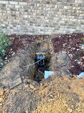 Excavated soil at brick exterior revealing installed steel pier bracket used for foundation repair