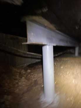 White support jack under wooden beam in a crawl space, installed to stabilize foundation and floor framing
