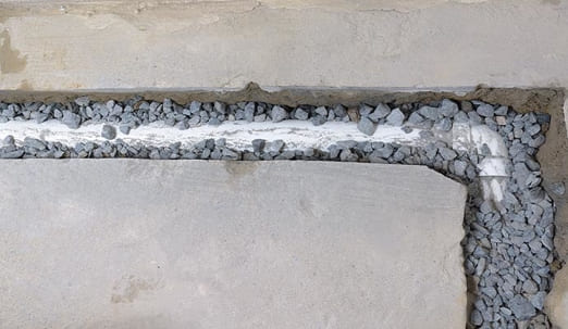 Perimeter PVC drain pipe in gravel-filled trench beside concrete slab for basement waterproofing and drainage