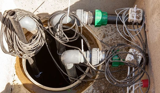 Sump pump basin with discharge pipes, check valves and sensor cables for basement drainage and waterproofing