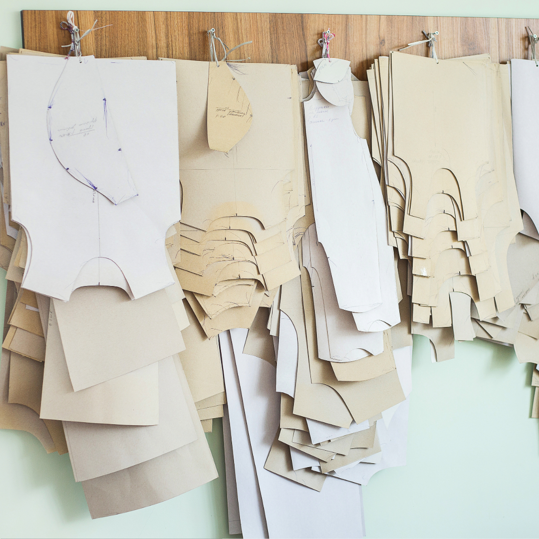 Cardboard patterns of garments, hanging on wall hooks in graded stacks. 