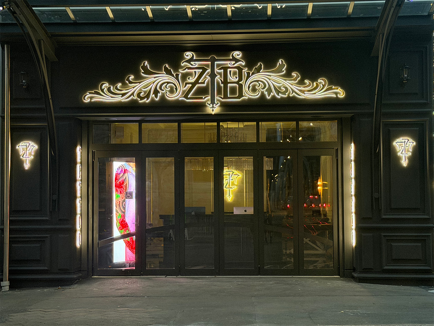 Entrance of a dark building with illuminated decorative signage featuring ornate initials above the door.