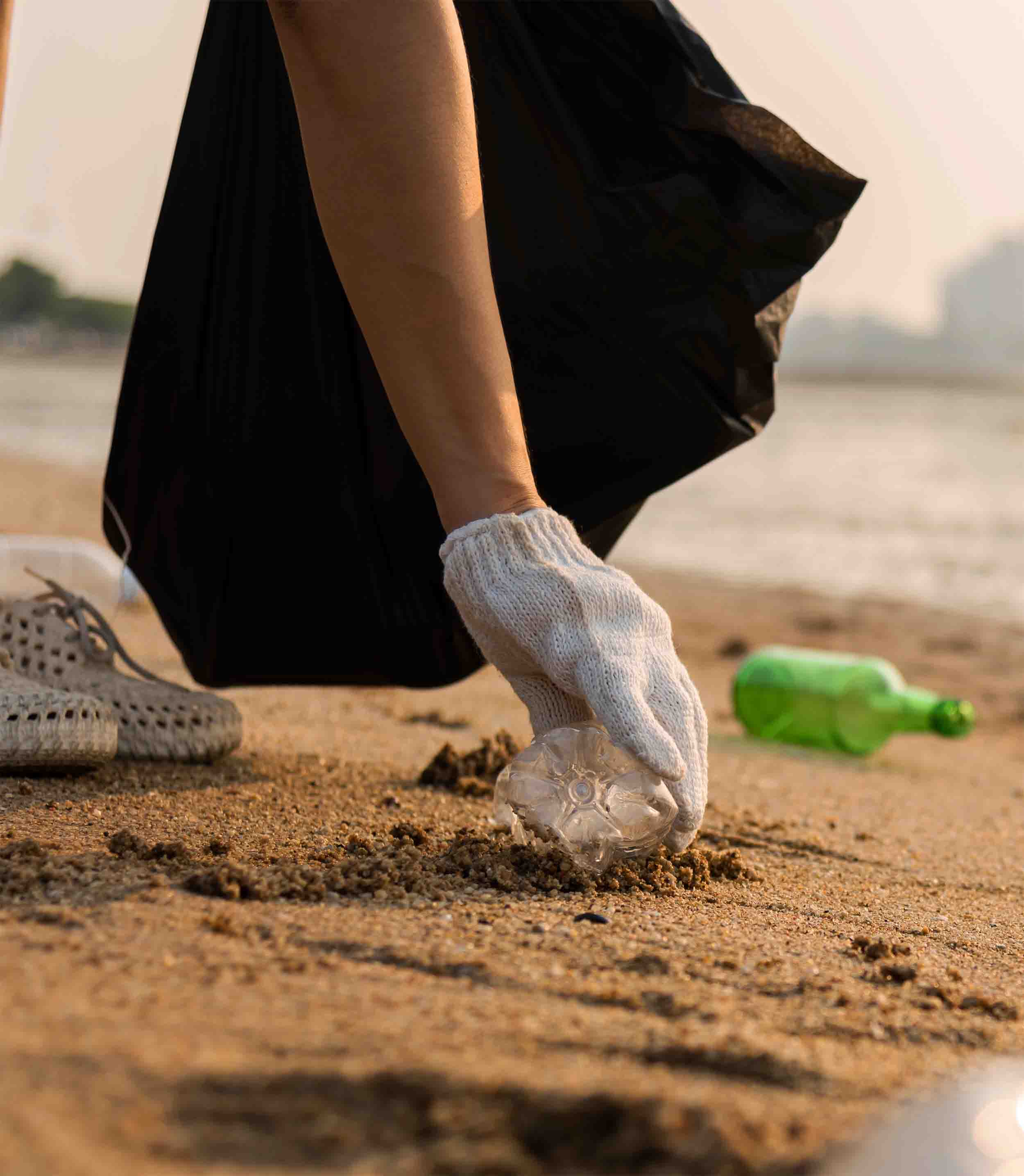 A hand picking up trash along the seaside.