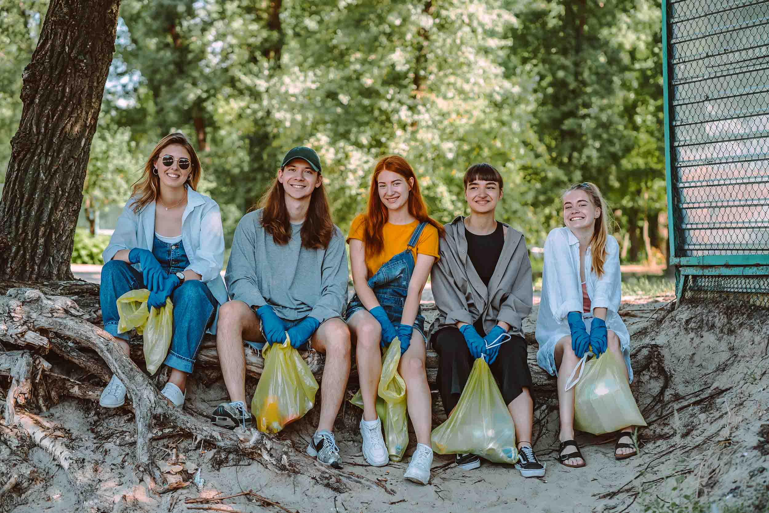 A group of people sitting in a row with their collected trash bags.