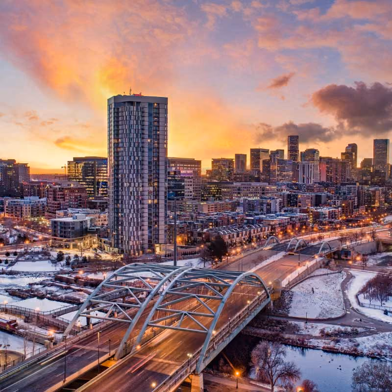 Aerial view of a cityscape at sunset with a prominent building and curved bridge in Denver, United States.