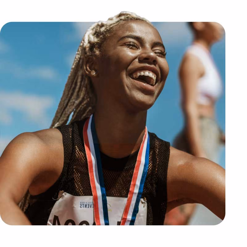 Athlete with braids wearing a medal and a race bib against a blue sky.