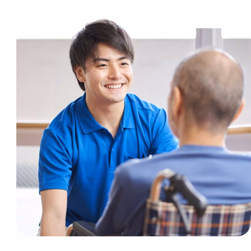 Person in blue shirt conversing with an elderly individual seated in a wheelchair.