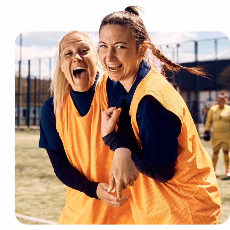 Two soccer players in orange bibs on a field, embracing in celebration.