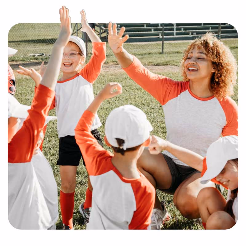 Youth soccer team in red and white uniforms celebrating with high fives on a field.