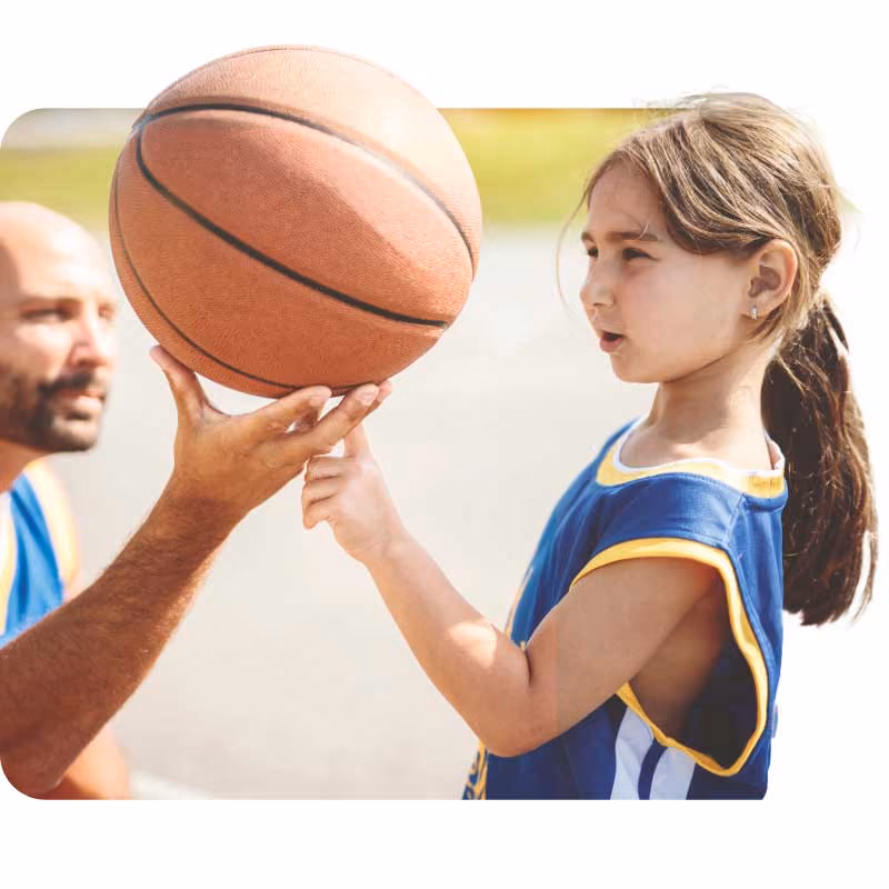A child in a basketball uniform reaches for a ball held by an adult.