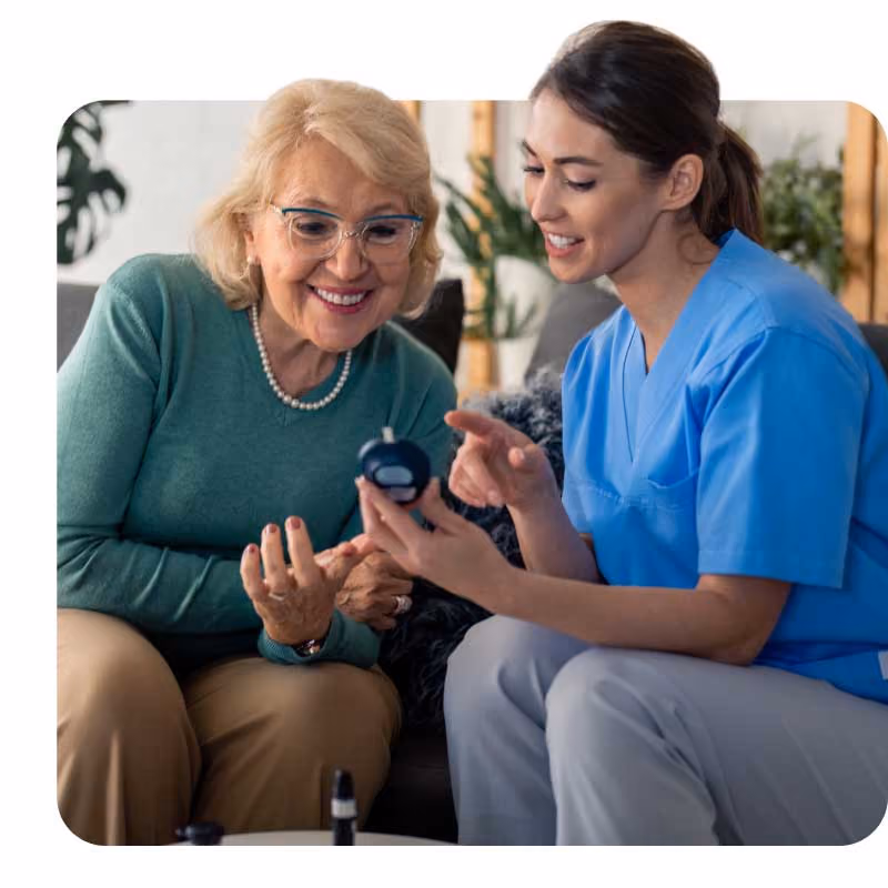 Nurse in scrubs showing a glucometer to an older woman.
