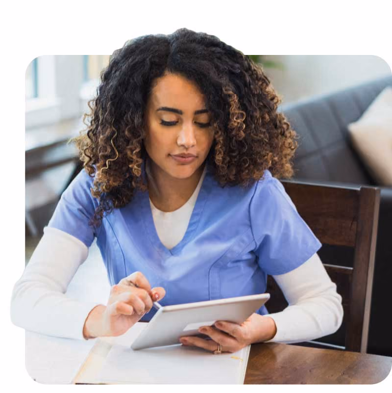 Healthcare professional in blue scrubs using a tablet at a table.
