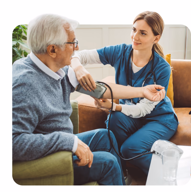 Nurse in blue scrubs giving a glass of water  and medication to a white-haired patient.