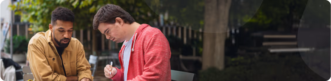 Disability Support Worker assisting participant with paperwork in a park.