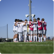 A soccer team in white and red uniforms huddled together on the field under a clear blue sky.