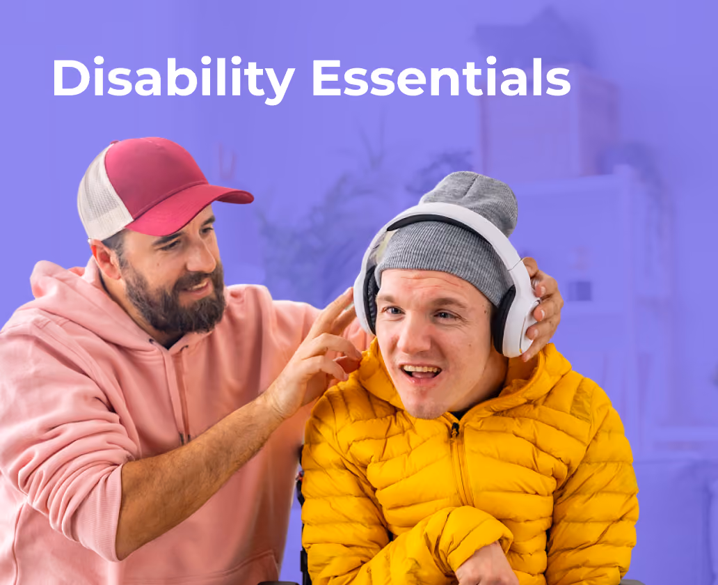 Man in a pink hoodie helps a smiling young man with headphones wearing a yellow jacket and gray beanie.