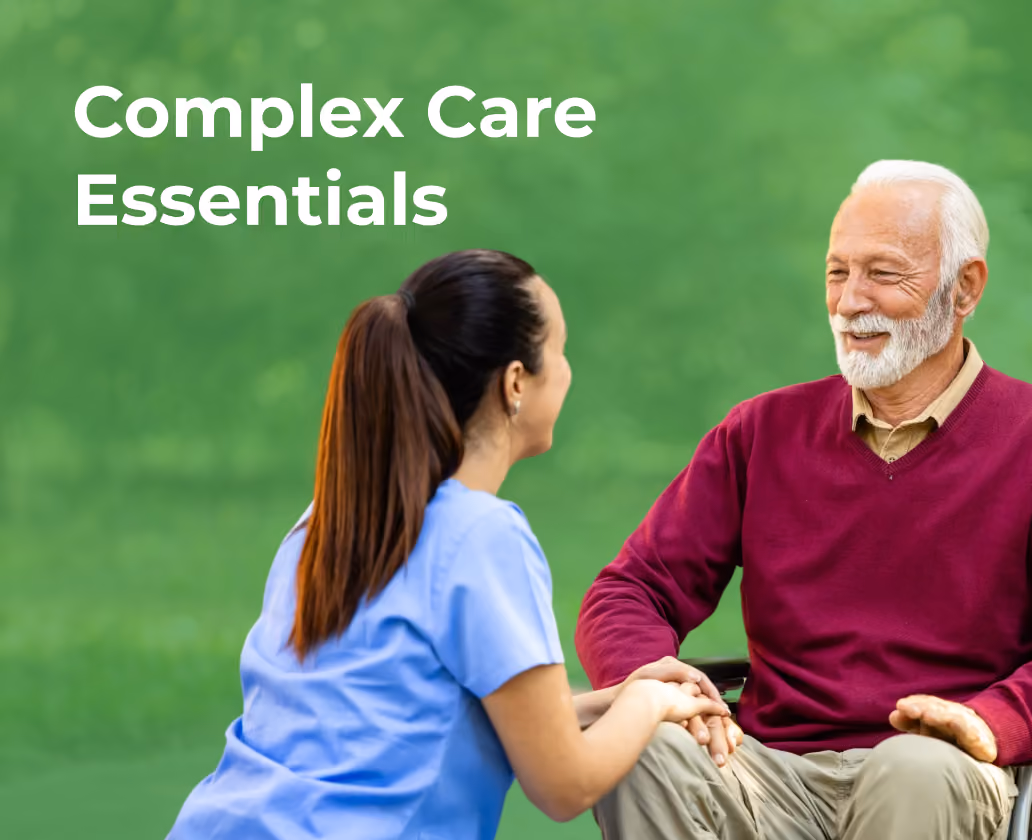Caregiver in scrubs holding hands and smiling with elderly man in a wheelchair on green background.