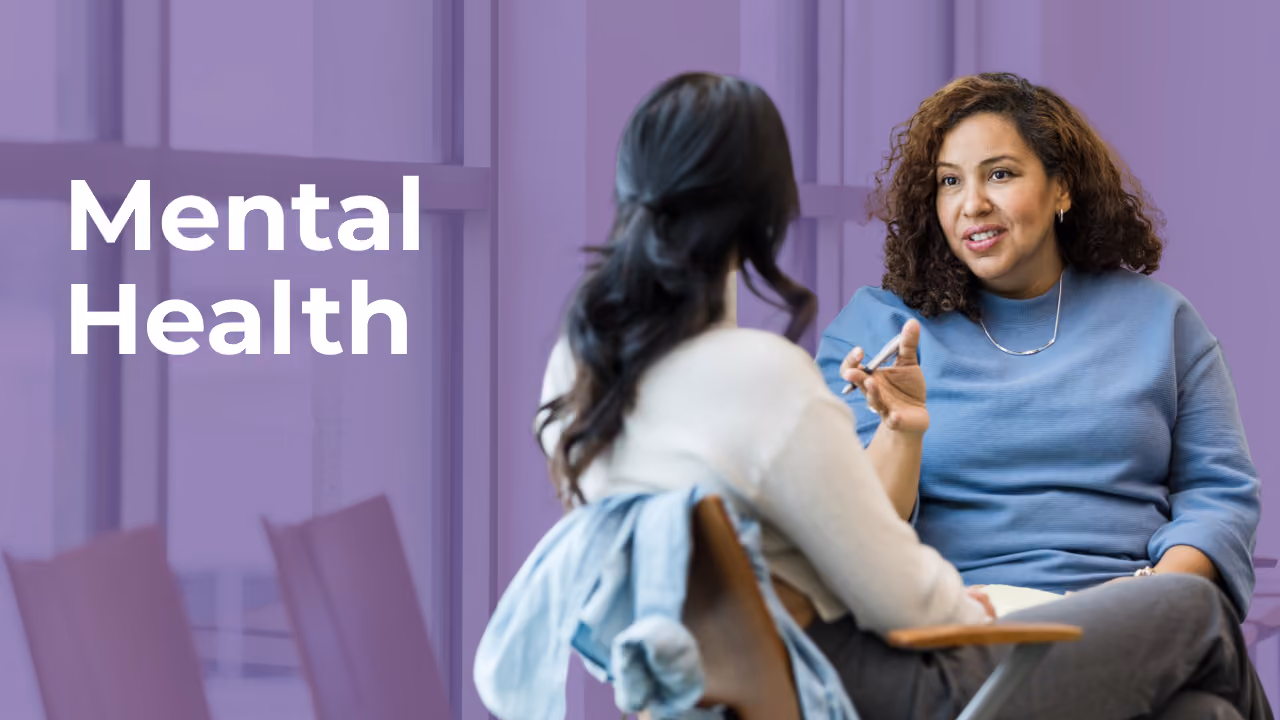 Two women having a conversation in an office setting with the words Mental Health on the side.