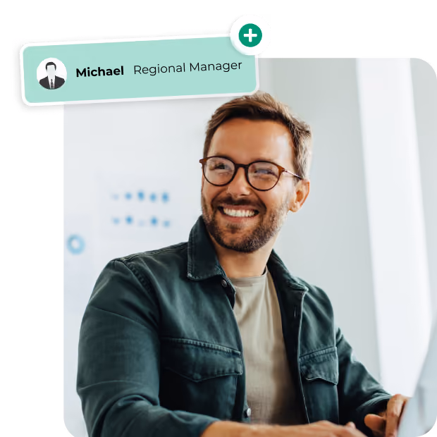 Smiling man wearing glasses and a green jacket sitting indoors with a name label saying Michael Regional Manager.