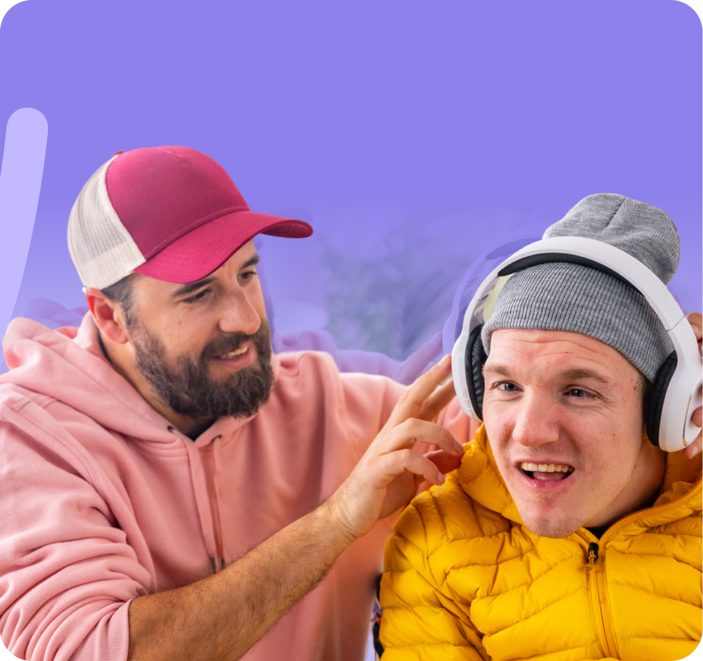 Man who is a support worker in a pink hoodie assisting his participant with putting on headphones