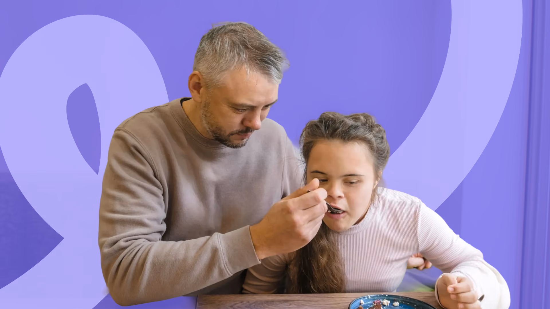 A man gently helps a young woman with Down syndrome eat from a spoon at a table, with a purple colour overlay.