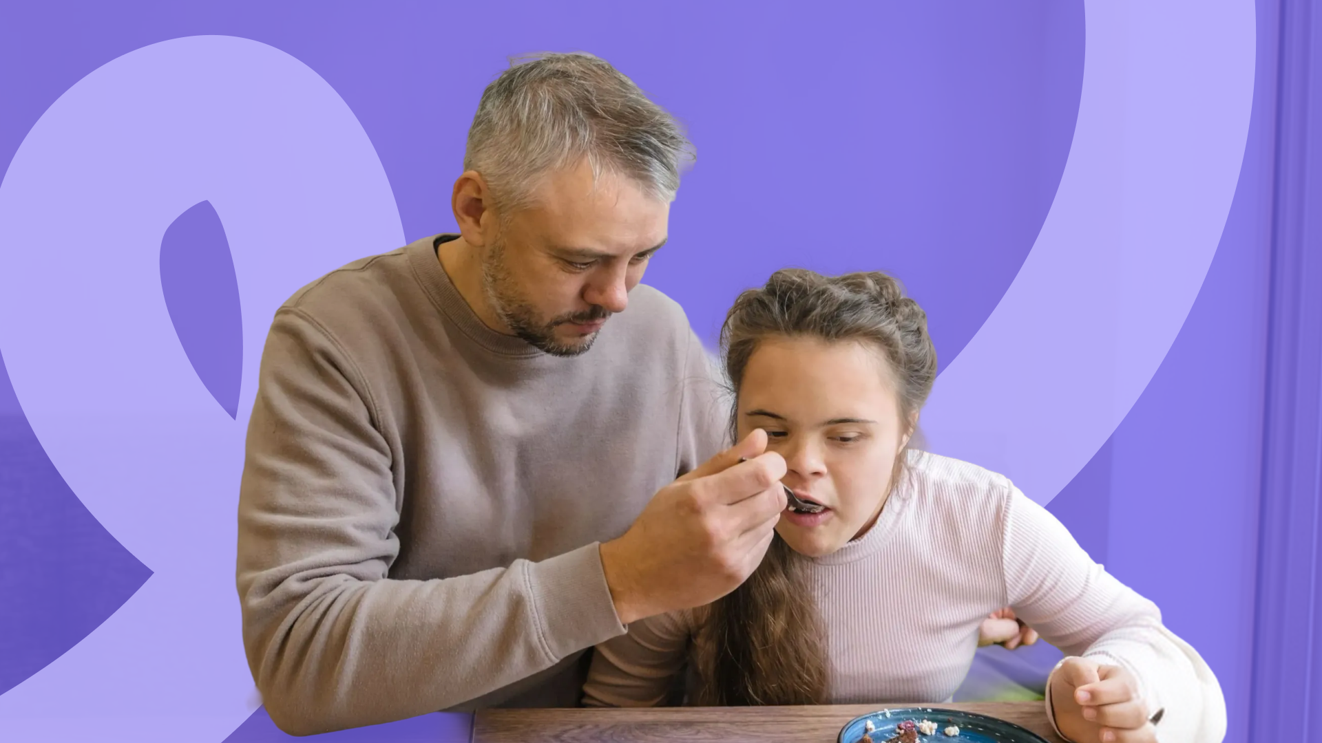 A man gently helps a young woman with Down syndrome eat from a spoon at a table, with a purple colour overlay.