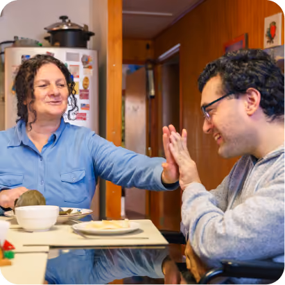 A woman and a man smile and high-five while sitting together in a kitchen.