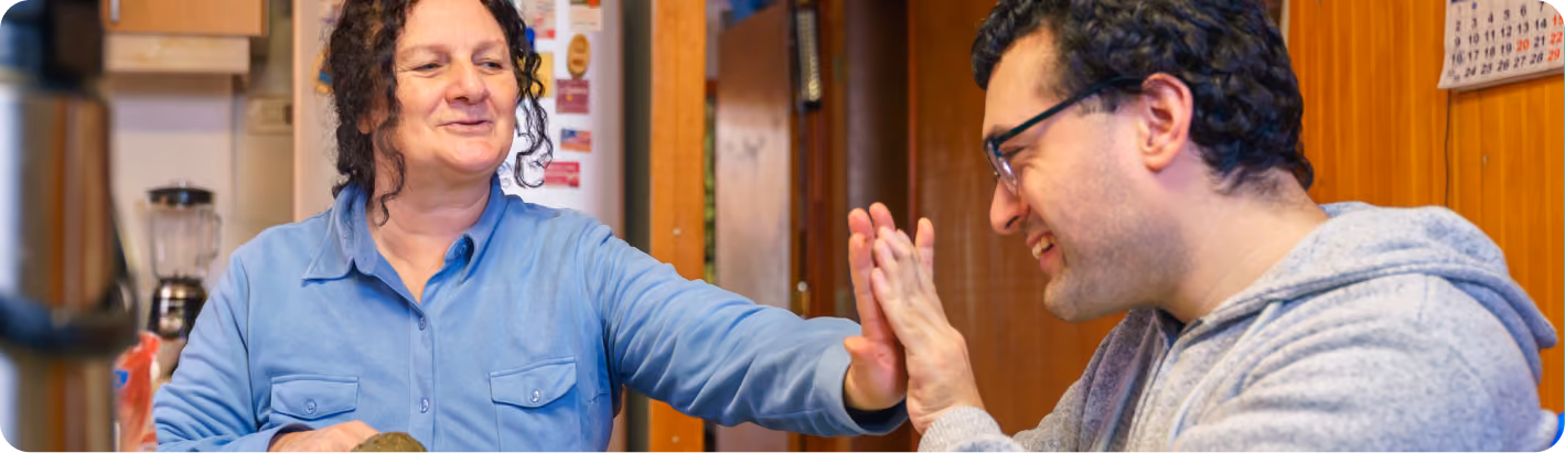 A woman and a man smile and high-five while sitting together in a kitchen.