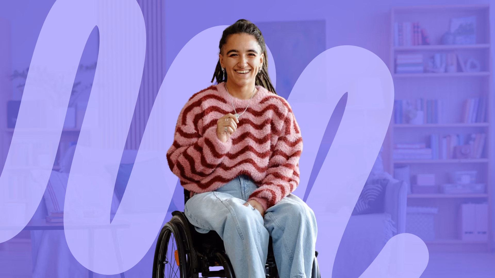 A smiling young woman with long dreadlocks, wearing a pink and red jumper, sitting in a manual wheelchair in a bright living room.