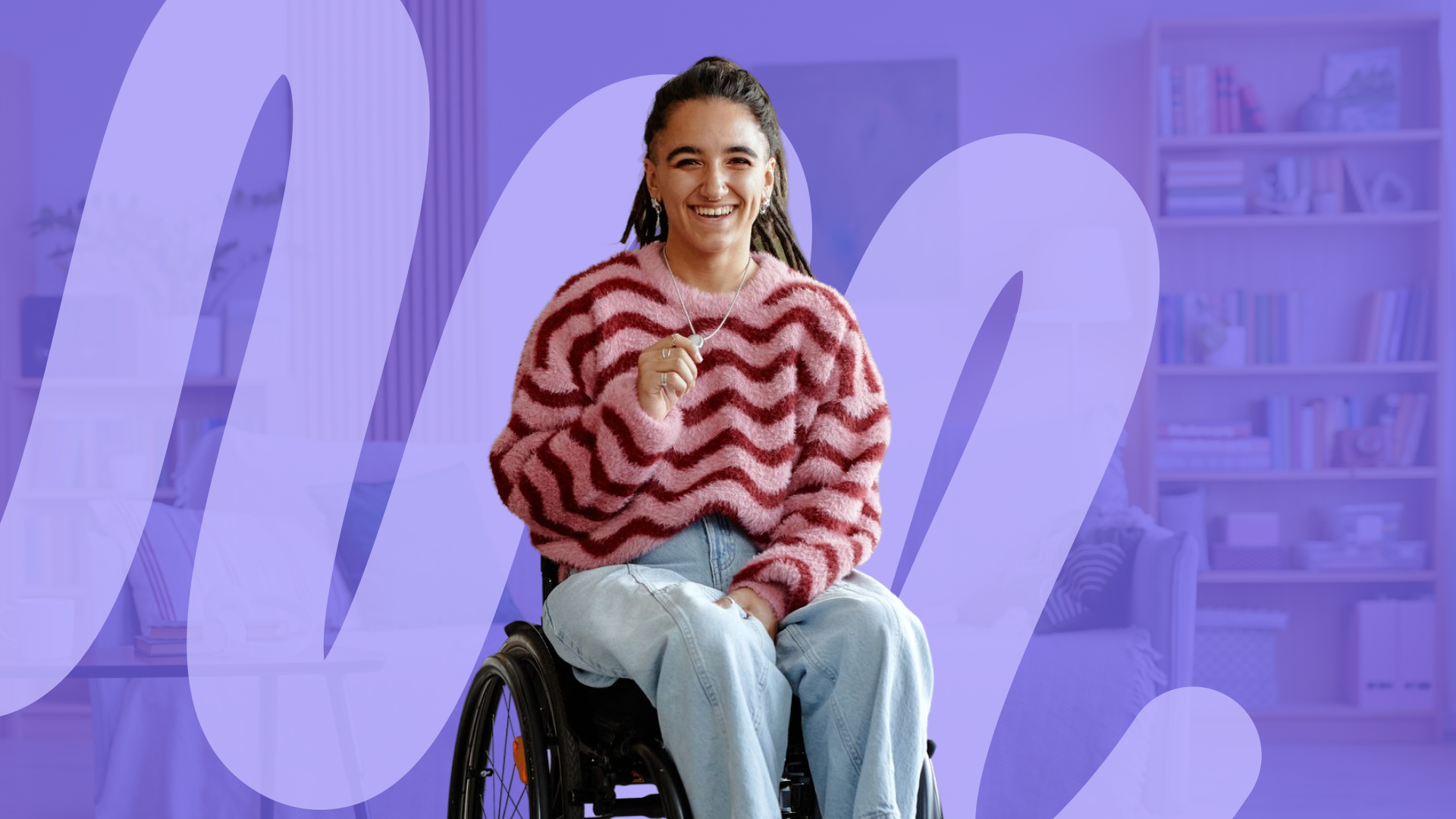 A smiling young woman with long dreadlocks, wearing a pink and red jumper, sitting in a manual wheelchair in a bright living room.