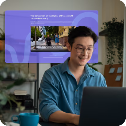 A man smiling while using a laptop at home, with a purple online training screen about the Convention on the Rights of Persons with Disabilities displayed behind him.