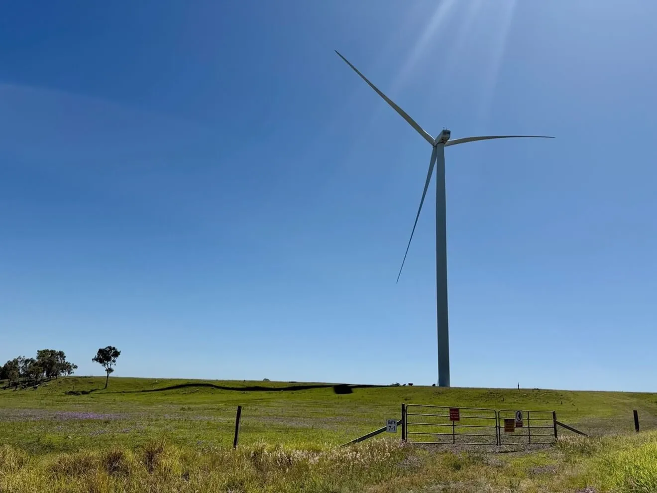 Large wind turbine on green farmland with farm gate and warning signs in foreground