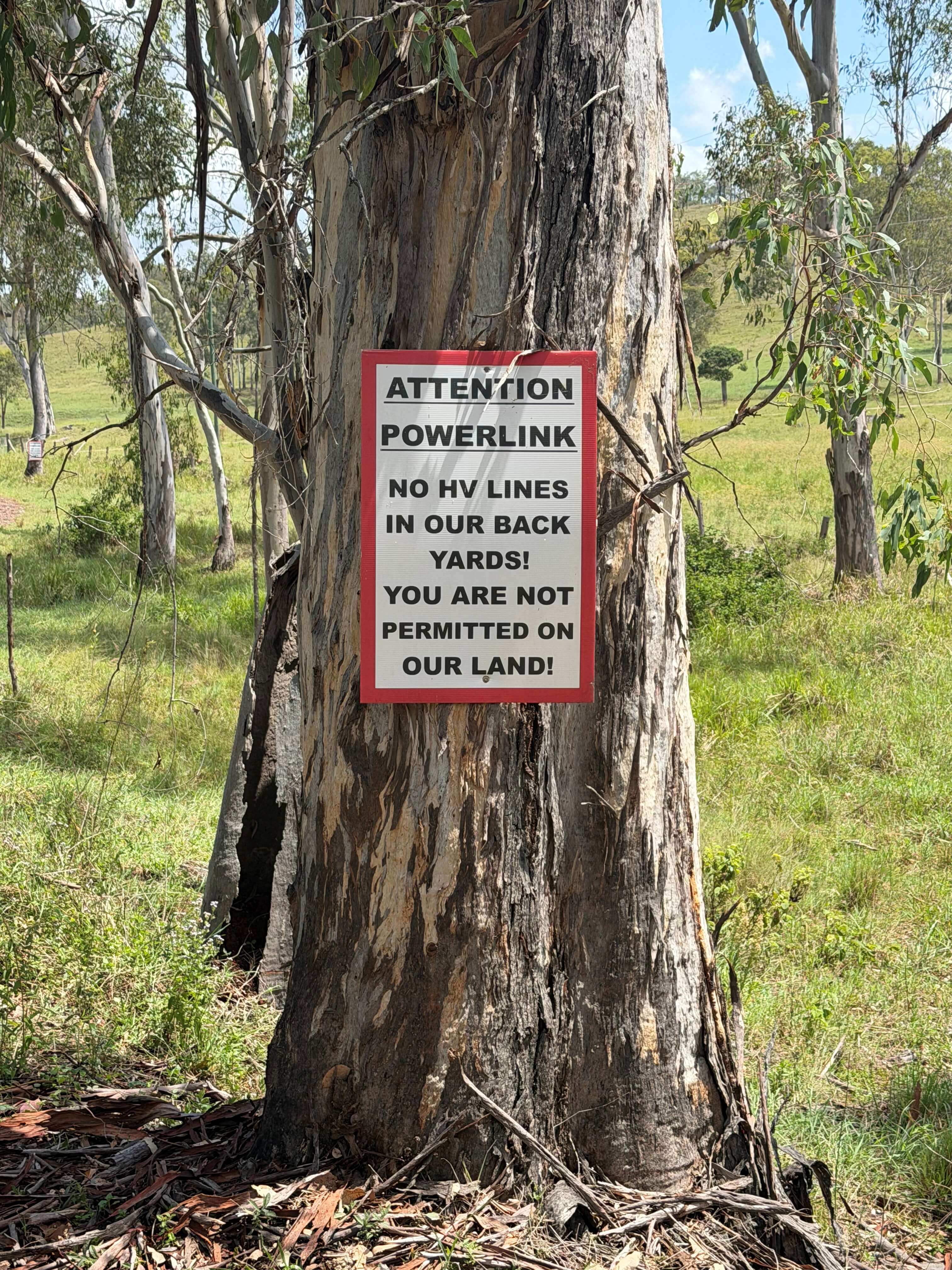  Warning sign nailed to a eucalyptus tree trunk reading Attention Powerlink with a message about access to private rural land