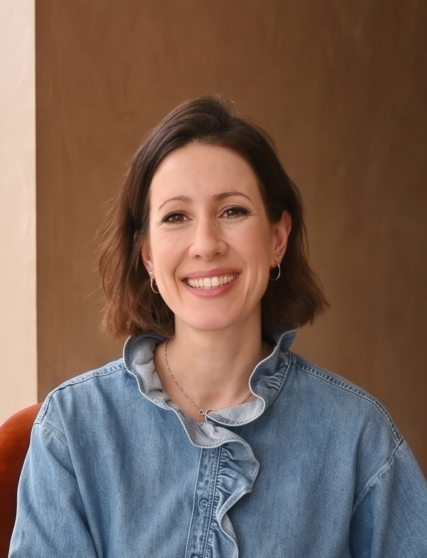 Smiling woman with short brown hair wearing a white sleeveless top and gold pendant necklace.