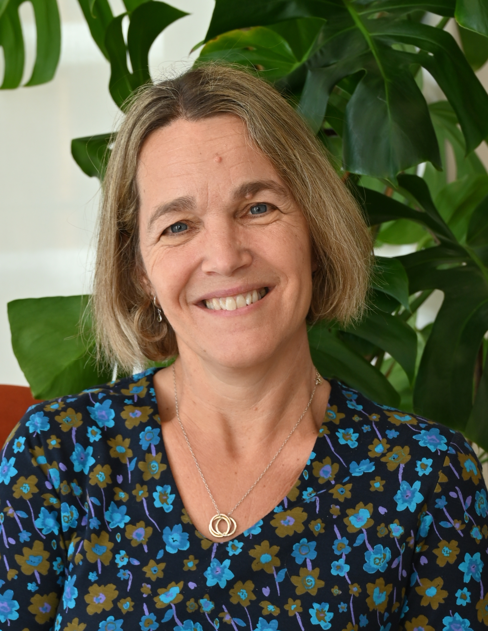 Smiling woman with short blonde hair wearing a green floral top and a silver necklace.