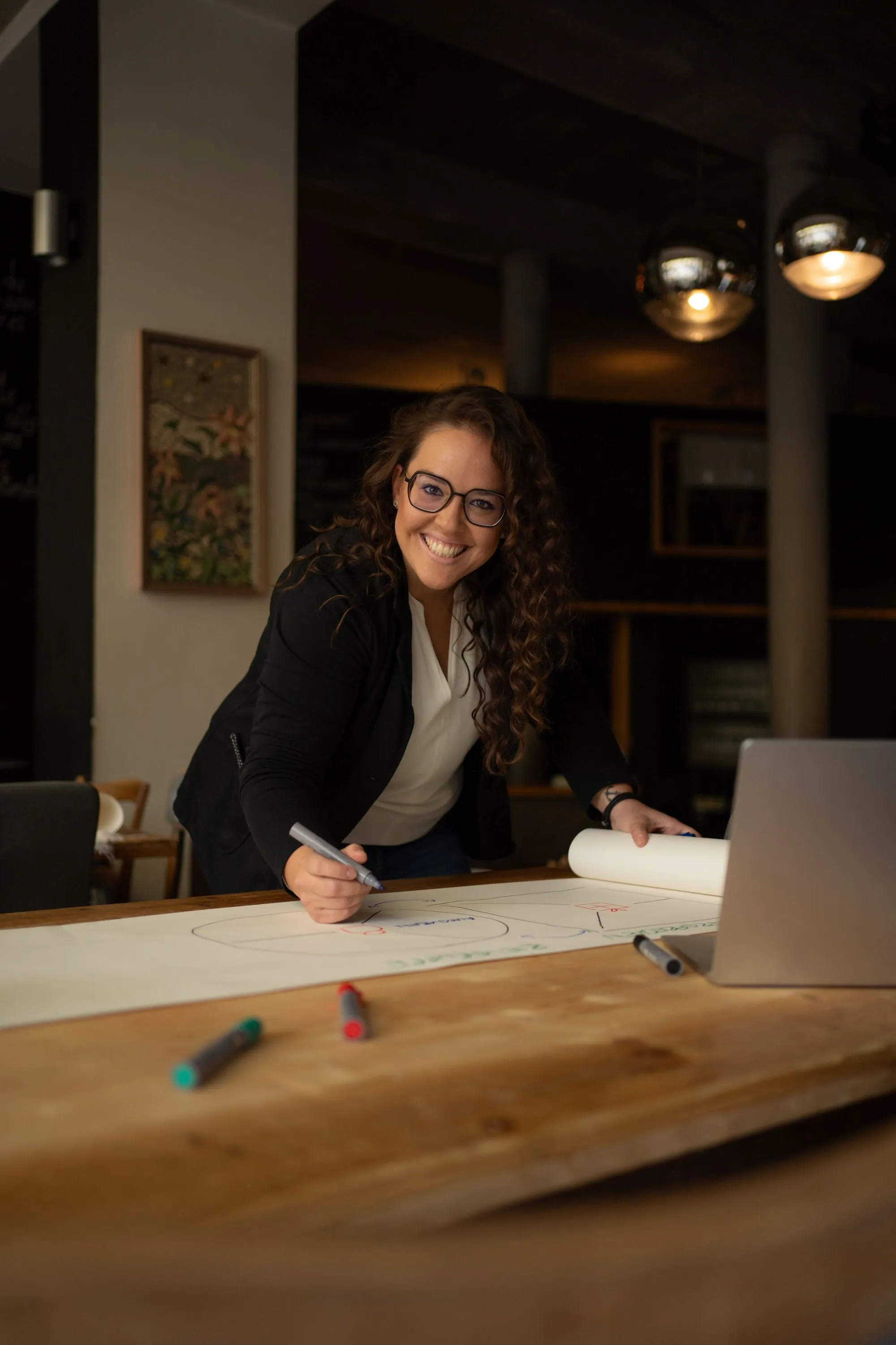 Lachende Frau bei der Arbeit an einem Konzept im modernen Büro, aufgenommen im Stil authentischer Corporate Fotografie.