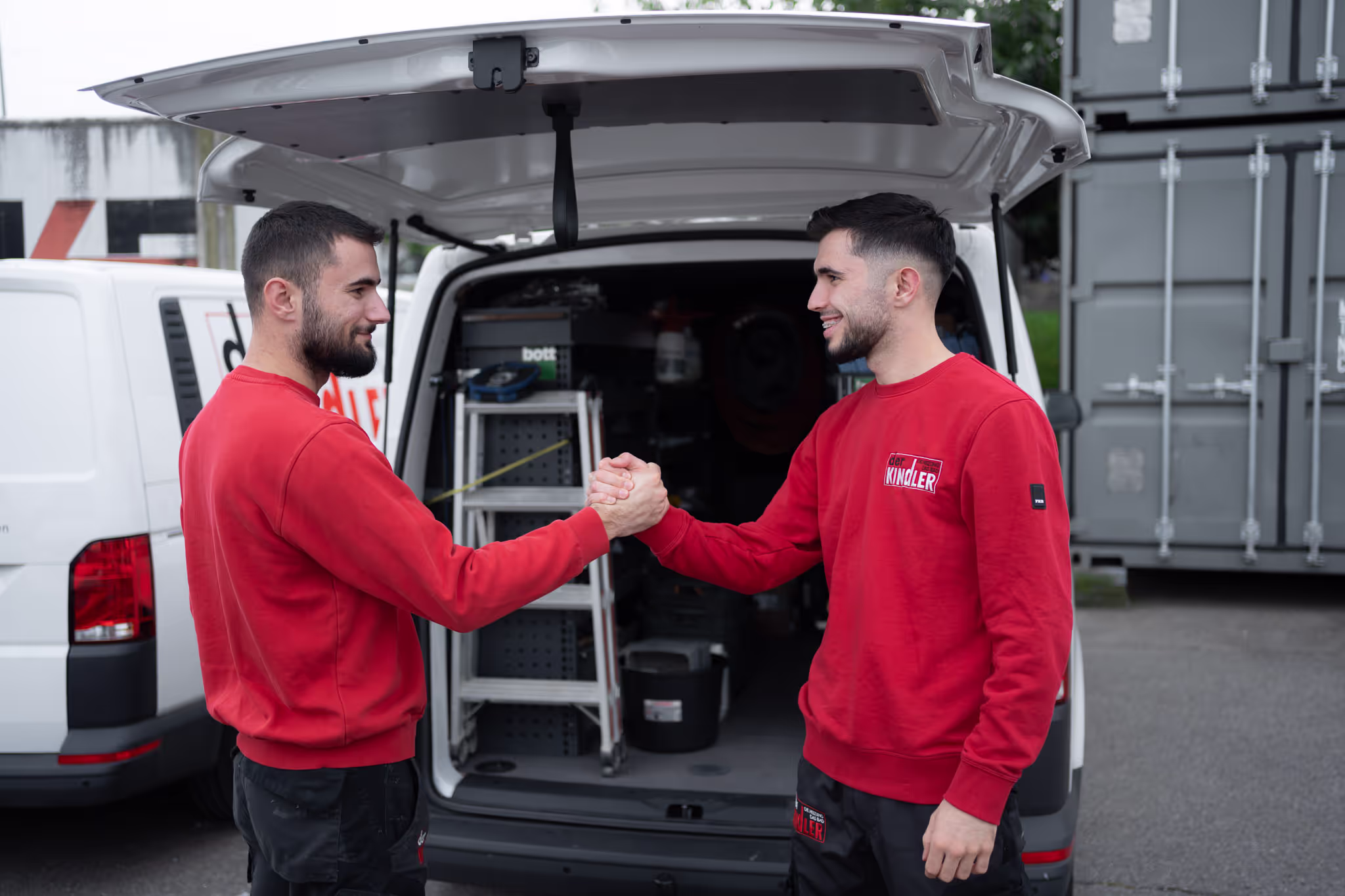 Zwei Mitarbeiter stehen vor einem Firmenfahrzeug und geben sich die Hand
