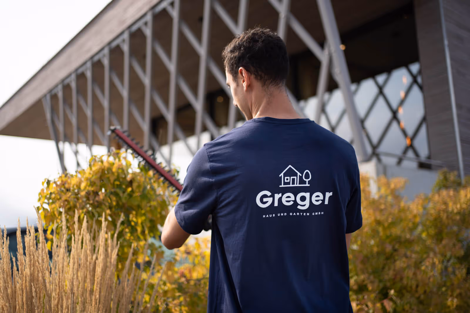 Corporate Fotograf dokumentiert die Arbeit eines Greger Haus und Garten Mitarbeiters beim Heckenschneiden vor einem modernen Firmengebäude.