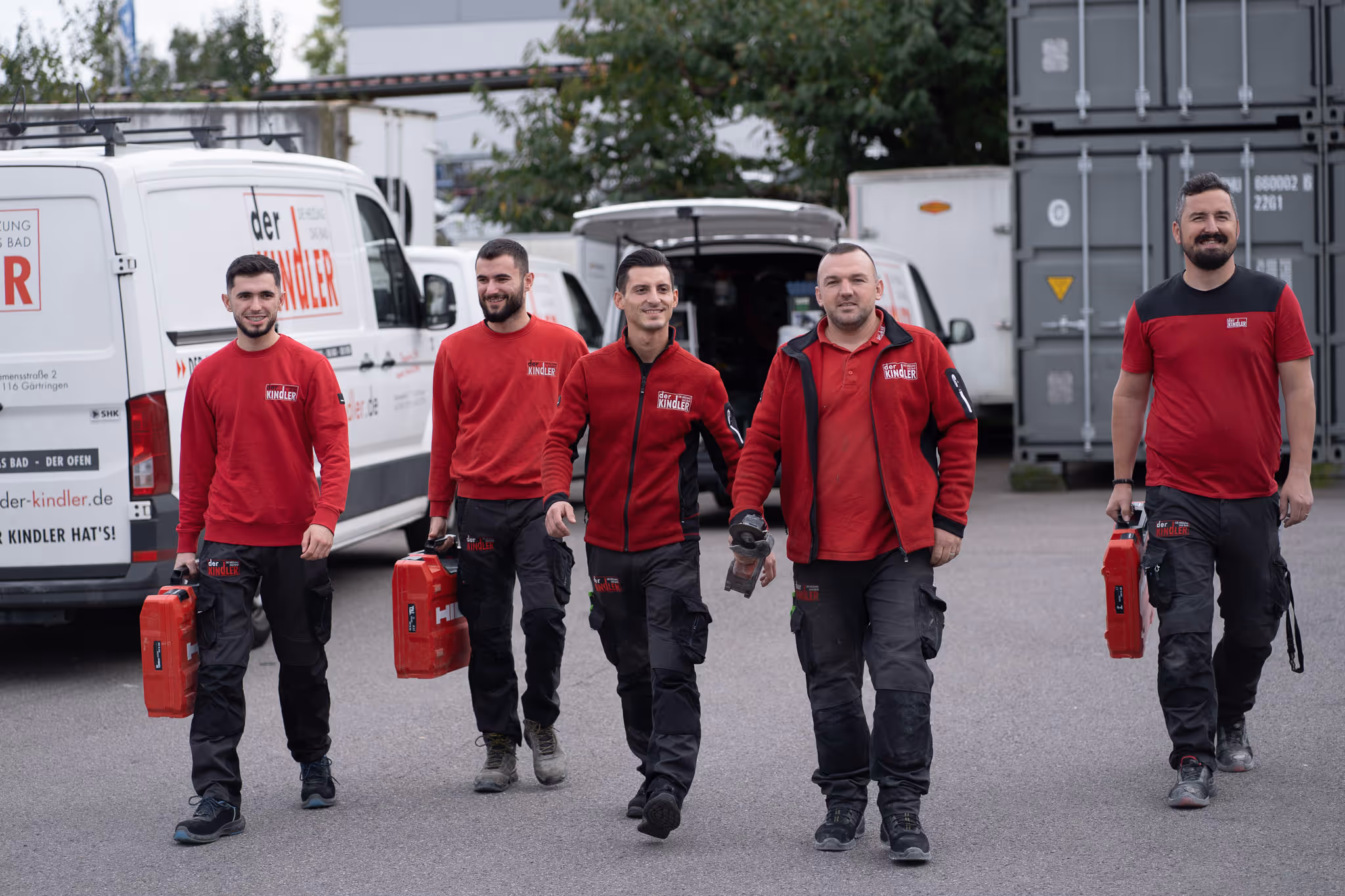 Fotograf & Videograf Rottweil dokumentiert Handwerkerteam in roter Arbeitskleidung, das mit Werkzeugkoffern über den Betriebshof läuft