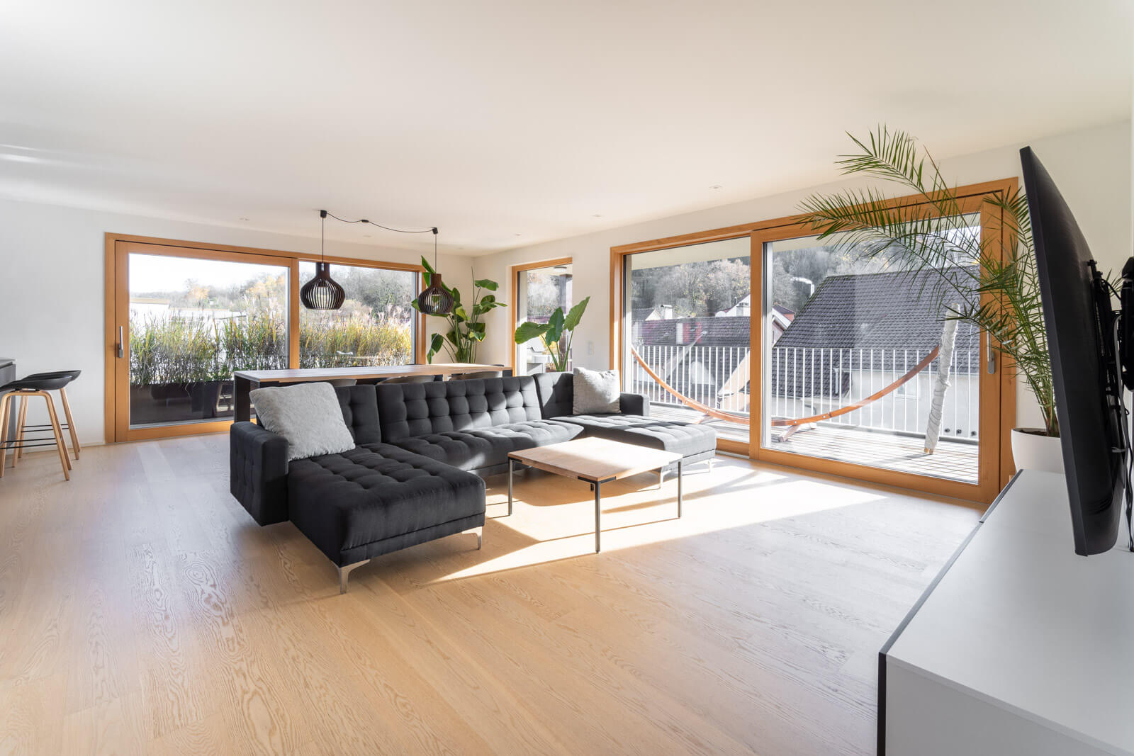 Helles, modernes Wohnzimmer mit großer Fensterfront, schwarzer Couch und Blick auf den Balkon