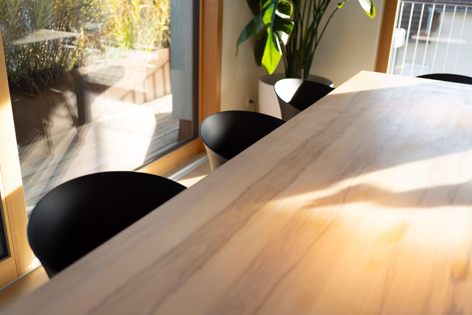 Detailaufnahme eines hellen Essbereichs mit großem Holztisch, schwarzen Designerstühlen und natürlicher Lichtstimmung